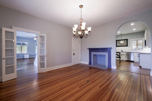 unfurnished living room with arched walkways, dark wood-style floors, recessed lighting, ceiling fan with notable chandelier, and french doors