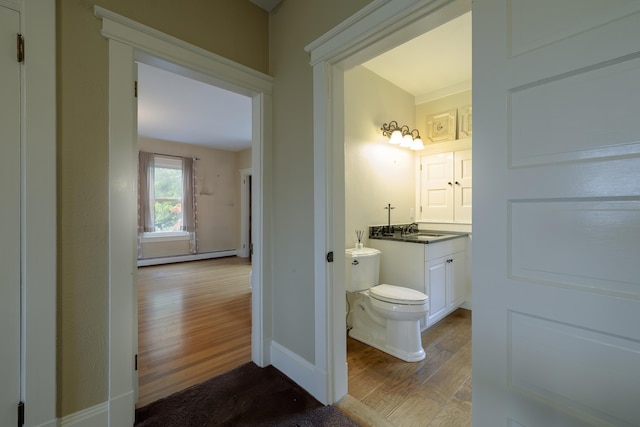 half bath with vanity, toilet, wood finished floors, a baseboard radiator, and baseboards
