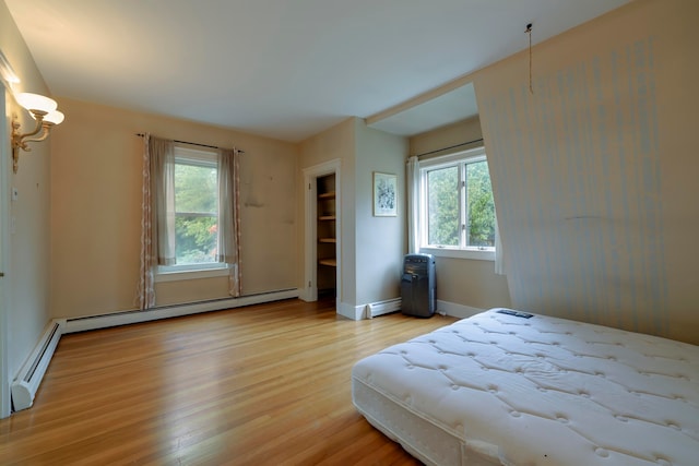 bedroom with a baseboard heating unit, light hardwood / wood-style flooring, and multiple windows