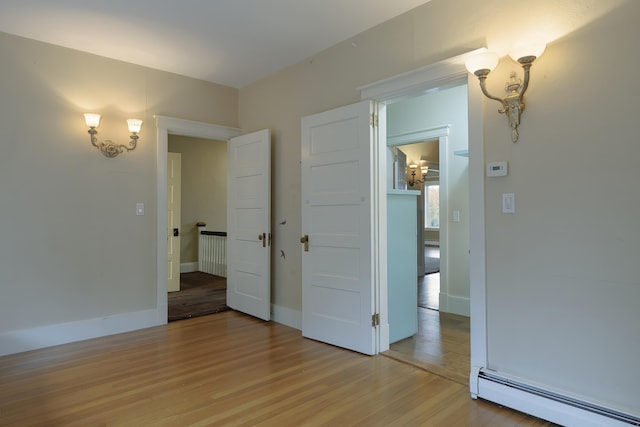 unfurnished bedroom with a baseboard radiator, light wood-type flooring, and baseboards