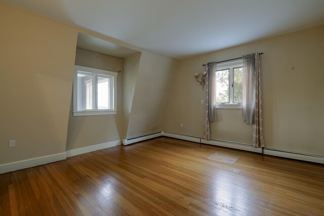 unfurnished room with wood finished floors, a baseboard heating unit, and baseboards