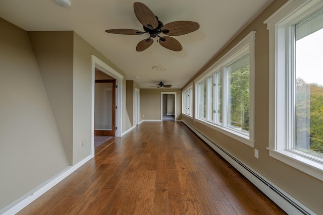 hallway with dark wood-style floors, a baseboard heating unit, baseboards, and a healthy amount of sunlight