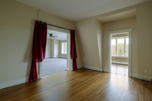 unfurnished room with baseboard heating, wood finished floors, and baseboards