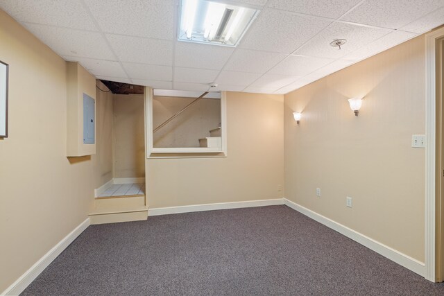 finished below grade area featuring a paneled ceiling, carpet flooring, baseboards, stairs, and electric panel