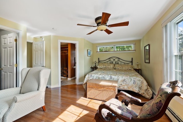 bedroom featuring a baseboard radiator, multiple windows, baseboards, and wood finished floors