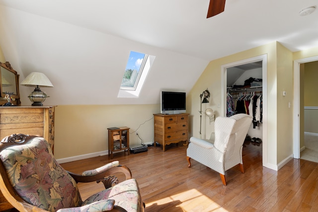 sitting room with vaulted ceiling with skylight, wood finished floors, and baseboards