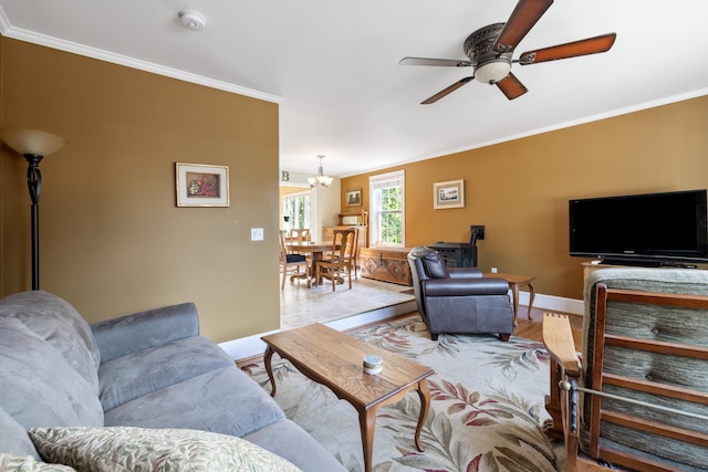 living area featuring light wood-style flooring, baseboards, crown molding, and ceiling fan with notable chandelier