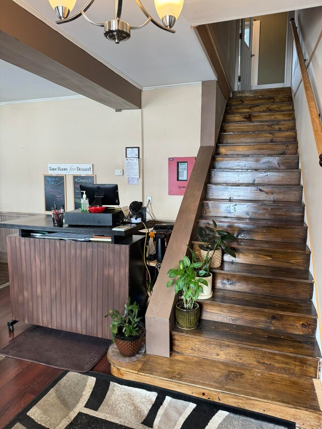 stairs featuring wood-type flooring, ornamental molding, and a notable chandelier