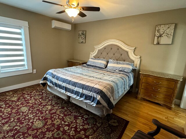 bedroom with a wall unit AC, ceiling fan, and hardwood / wood-style floors