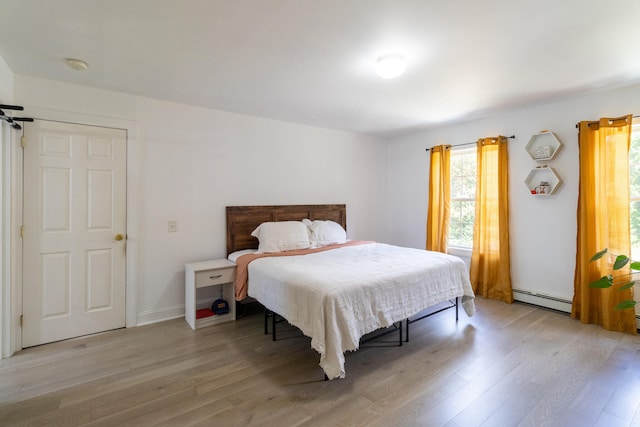 bedroom with light hardwood / wood-style flooring and a baseboard heating unit