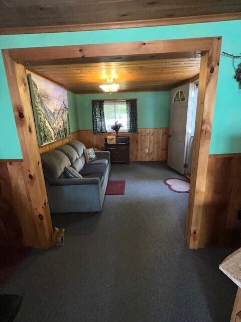living room featuring wood ceiling, wood walls, wainscoting, and carpet