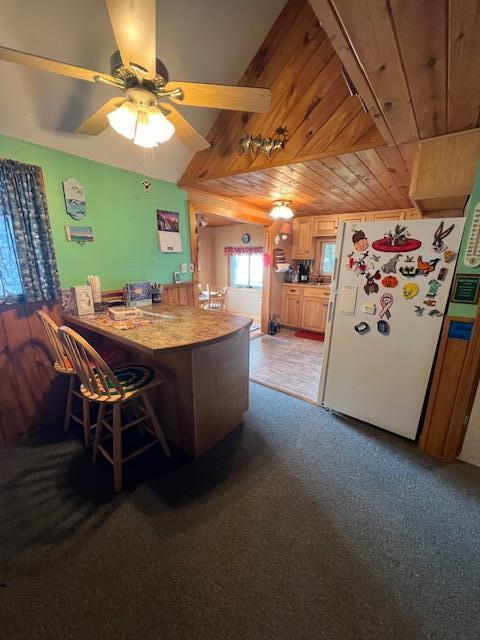 kitchen with freestanding refrigerator, ceiling fan, a kitchen bar, a peninsula, and wood ceiling