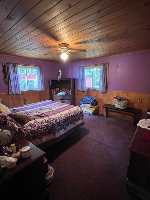 carpeted bedroom with wood ceiling, wood walls, a ceiling fan, and a wainscoted wall