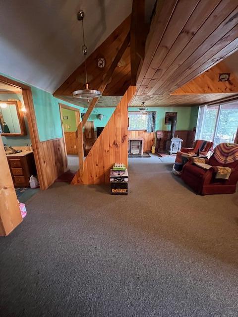 carpeted living area with a wood stove and wooden walls