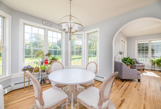 dining room with a baseboard radiator, light wood-type flooring, a chandelier, and a healthy amount of sunlight