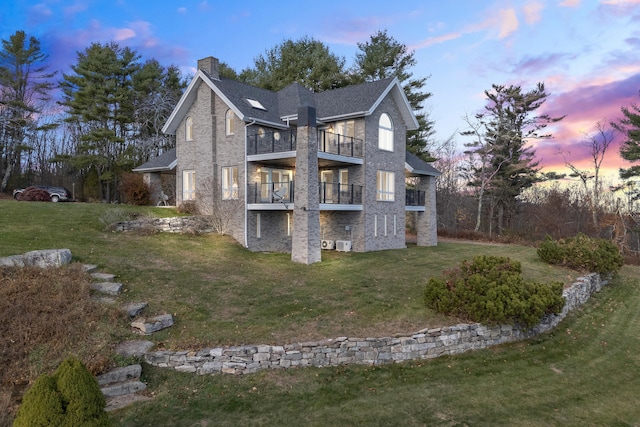 property exterior at dusk featuring a balcony and a lawn