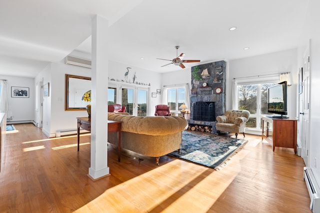 living room featuring a stone fireplace, baseboard heating, a wall mounted AC, and light hardwood / wood-style flooring