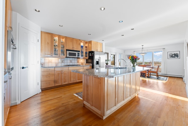 kitchen featuring light stone countertops, stainless steel appliances, a center island with sink, and light hardwood / wood-style floors