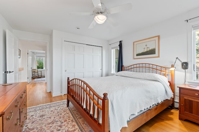 bedroom with ceiling fan, baseboard heating, light hardwood / wood-style flooring, and a closet