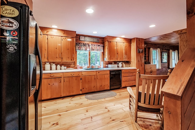 kitchen featuring black appliances, light hardwood / wood-style floors, wood walls, and sink