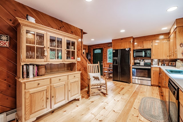 kitchen featuring light wood-type flooring, black appliances, wood walls, and a baseboard heating unit