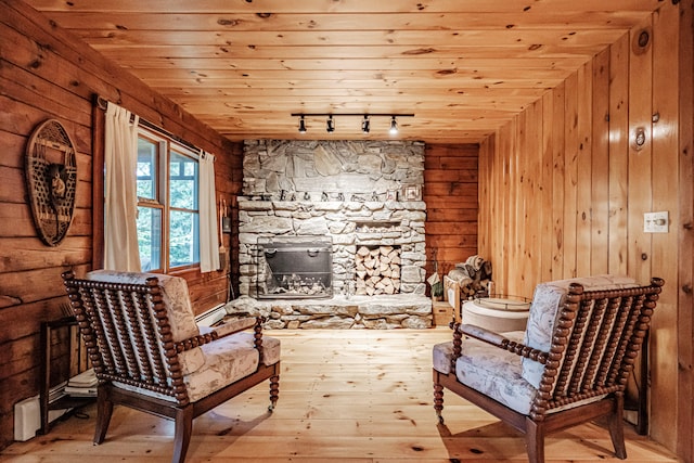 living area with wood ceiling, a stone fireplace, baseboard heating, light hardwood / wood-style flooring, and wooden walls