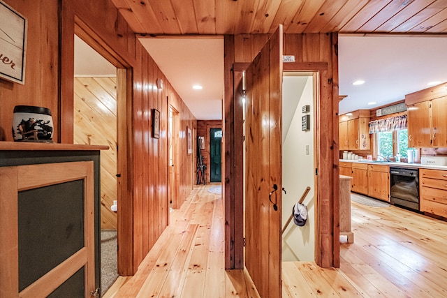 hallway featuring light wood-type flooring, wood ceiling, and wooden walls