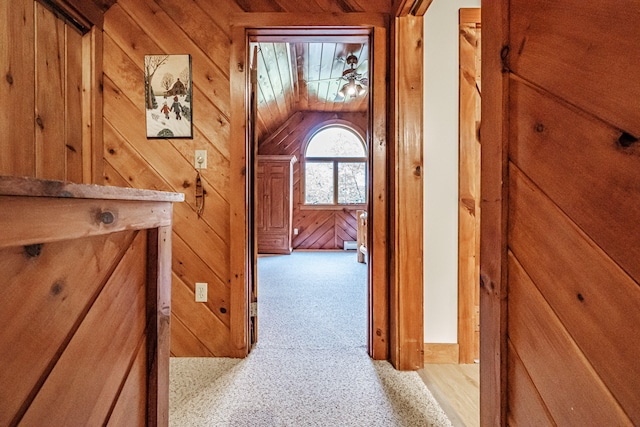 hallway with lofted ceiling, wood walls, and light carpet