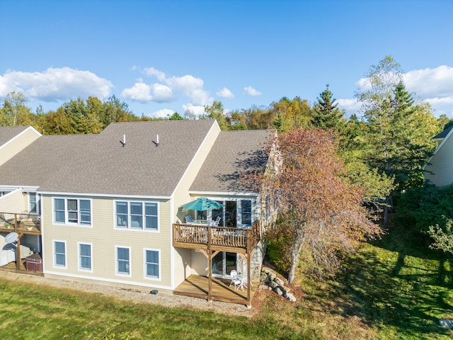 back of property featuring a wooden deck, a lawn, and roof with shingles