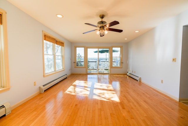 empty room featuring a baseboard radiator, baseboards, and light wood finished floors