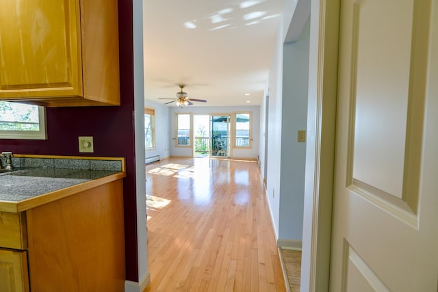 hall with light wood finished floors, a baseboard radiator, and baseboards