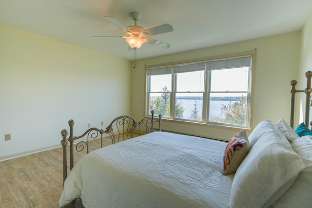 bedroom with a water view, ceiling fan, baseboards, and wood finished floors