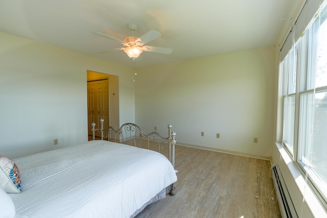 bedroom with light wood-type flooring, a baseboard radiator, baseboards, and a ceiling fan