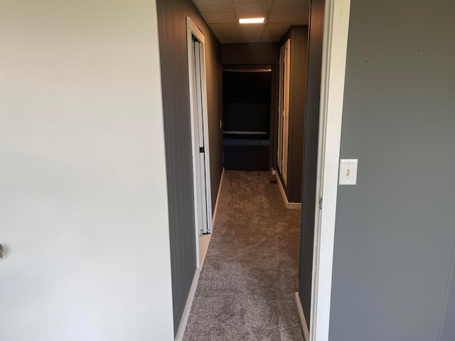 corridor featuring dark colored carpet and a paneled ceiling