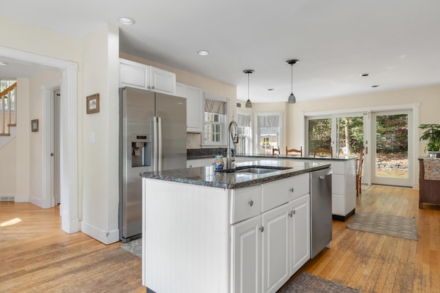 kitchen with pendant lighting, a kitchen island with sink, white cabinetry, light hardwood / wood-style flooring, and stainless steel appliances