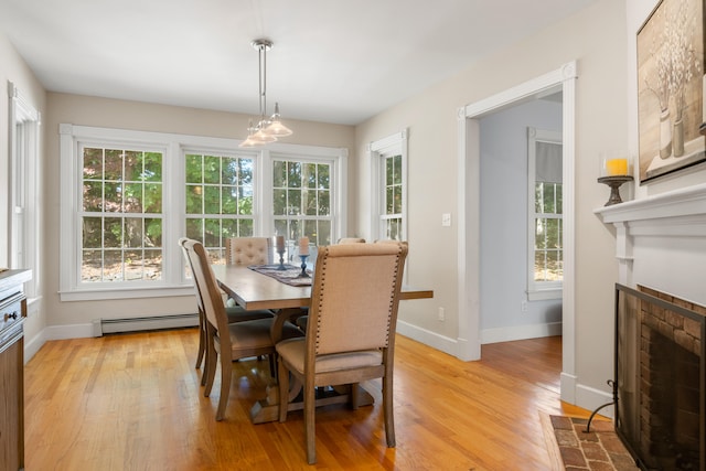 dining room featuring a brick fireplace, light hardwood / wood-style flooring, and a baseboard heating unit