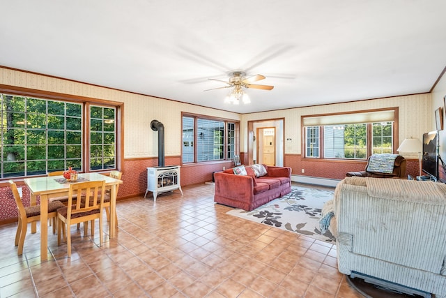 living room with ceiling fan, crown molding, a wood stove, and a wealth of natural light