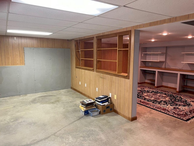 basement featuring carpet flooring, a drop ceiling, and wood walls