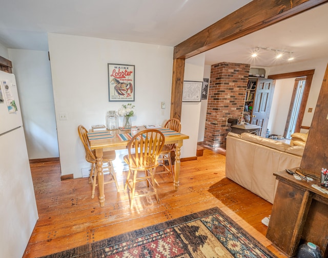 dining room featuring decorative columns, hardwood / wood-style flooring, beamed ceiling, and track lighting