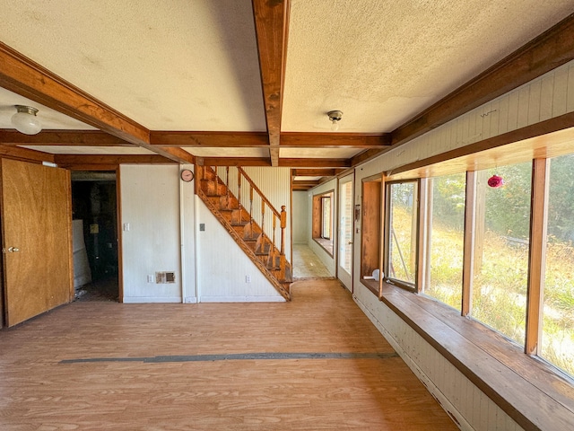 spare room featuring wooden walls, a textured ceiling, beamed ceiling, and hardwood / wood-style floors