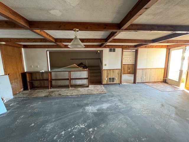 unfurnished living room with concrete flooring, beamed ceiling, a textured ceiling, and wooden walls