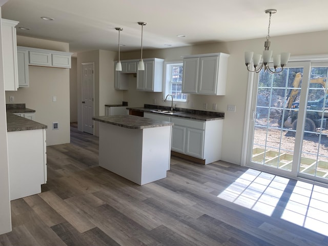 kitchen featuring a center island, wood finished floors, a sink, dark countertops, and a notable chandelier