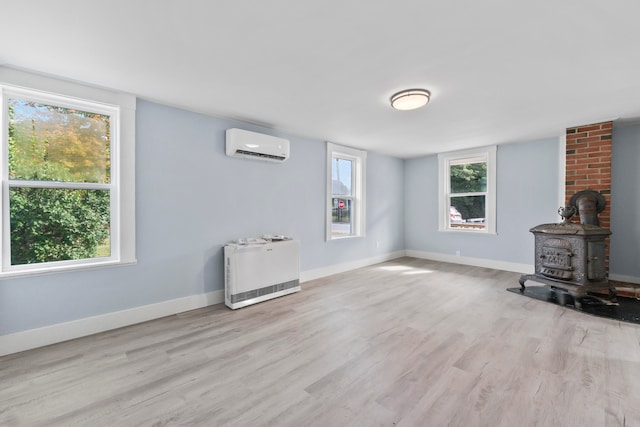 unfurnished living room featuring light hardwood / wood-style floors, a wood stove, and a wall unit AC