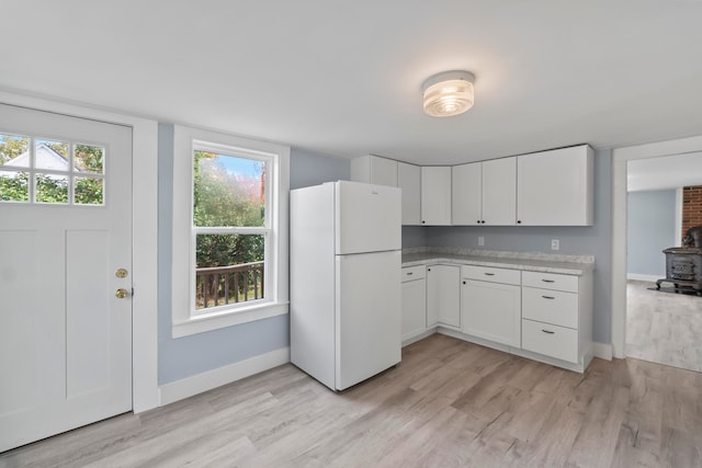 kitchen with white cabinets, light wood-type flooring, white fridge, and a wood stove