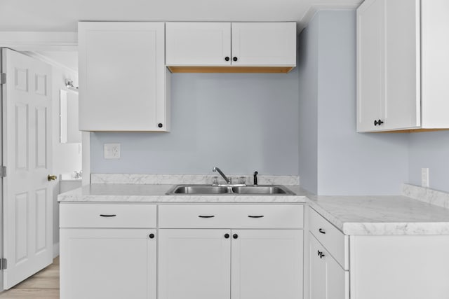 kitchen with white cabinets, light hardwood / wood-style floors, crown molding, and sink