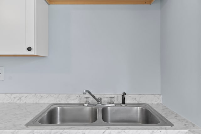 kitchen featuring light stone countertops, sink, and white cabinetry