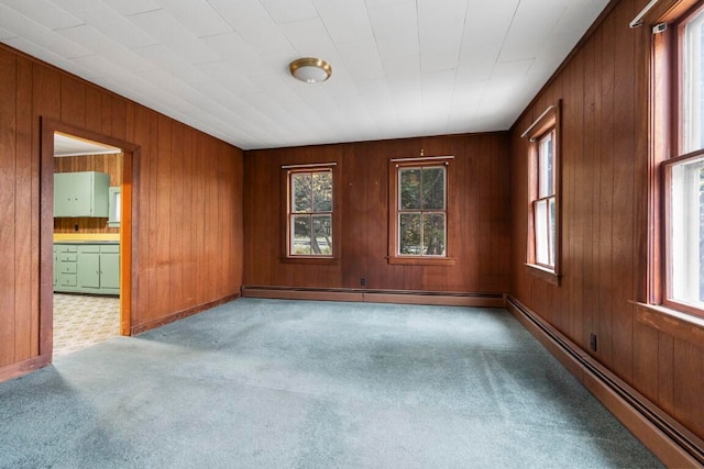 carpeted empty room with wooden walls, a baseboard heating unit, and a wealth of natural light