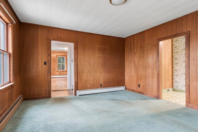 spare room with light colored carpet, a baseboard radiator, and wood walls