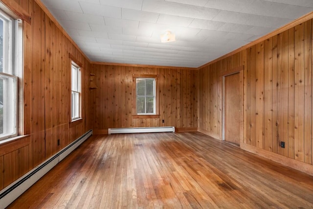 empty room with wooden walls, a baseboard heating unit, and hardwood / wood-style flooring