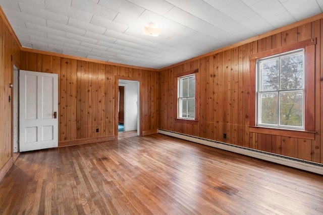 spare room with wood-type flooring, wooden walls, crown molding, and baseboard heating